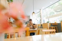 Mensajería de texto empresaria femenina en el teléfono inteligente sosteniendo la taza de café mientras está sentado en la cafetería - foto de stock