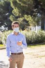 Бизнесмен в защитной маске с помощью мобильного телефона, стоя на тропинке — стоковое фото