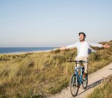 Homme insouciant avec les bras tendus vélo d'équitation à la plage contre ciel clair — Photo de stock