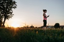 Female athlete using smart phone while standing on grass during sunset — Stock Photo