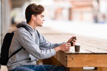 Красивый мужчина слушает музыку, используя смартфон, сидя в кафе на тротуаре — стоковое фото
