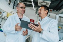 Учені, які посміхаються, стоячи в лабораторії, використовують цифрову табличку. — стокове фото