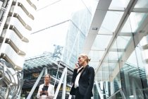 Smiling businesswoman talking on mobile phone while standing near female professional in financial district — Stock Photo