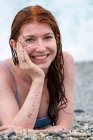 Mulher sorridente com cara de cascalho e areia deitada na praia — Fotografia de Stock