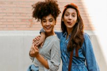 Young woman sticking tongue out while standing with friend against wall — Stock Photo