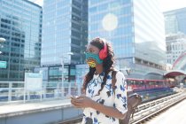 Businesswoman wearing face mask and headphones looking away while standing at station — Stock Photo