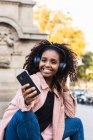 Smiling fashionable young woman taking selfie while listening music in city — Stock Photo
