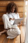 Smiling woman taking on video call through digital tablet while sitting by window at home — Stock Photo