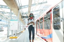 Businesswoman wearing face mask using mobile phone while standing at station platform — Stock Photo
