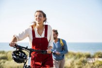 Усміхаючись з дівчиною на велосипеді, коли вона ходила з хлопцем проти моря. — стокове фото
