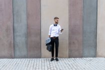 Бизнесмен пользуется смартфоном, стоя у стены — стоковое фото