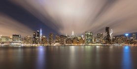 USA, New York, New York City, Midtown Manhattan skyline illuminated at night seen across river - foto de stock