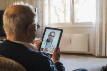 Uomo anziano che riceve consigli da un medico maschio in videochiamata tramite tablet digitale a casa — Foto stock