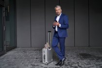Бизнесмен с помощью мобильного телефона, стоя с багажом на тропинке — стоковое фото