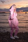 Porträt einer jungen Frau im rosafarbenen Kapuzenshirt, die bei Sonnenuntergang am Strand steht — Stockfoto
