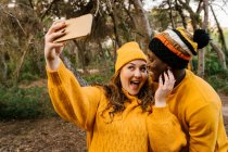 Веселая женщина делает селфи через мобильный телефон, стоя в лесу — стоковое фото
