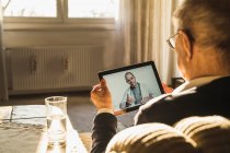 Medico maschio che consulta l'uomo anziano in videochiamata tramite tablet digitale in soggiorno — Foto stock