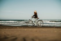 Junge Frau zu Fuß mit Fahrrad durch Wasserwellen am Fangar-Strand, ebro delta, Spanien — Stockfoto