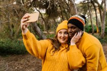 Young woman wearing knit hat taking selfie through mobile phone while standing at forest — Stock Photo