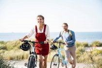 Lächelnder Mann und Frau zu Fuß mit Fahrrädern am Strand — Stockfoto