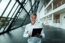 Uomo d'affari sorridente utilizzando tablet digitale nel corridoio ufficio — Foto stock