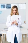 Усміхнений медичний працівник використовує цифровий планшет, стоячи навпроти столу — стокове фото