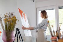 Молодая художница держит холст, стоя в домашней студии — стоковое фото