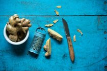 Radice di zenzero, grattugia e coltello da cucina sdraiato su una superficie di legno blu — Foto stock