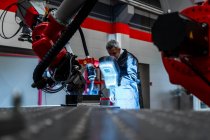 Welder with welding helmet examining robotics in factory — Stock Photo