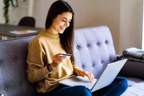 Young woman with credit card shopping over laptop while sitting at home — Stock Photo