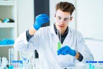 Giovane scienziato miscelazione di sostanze chimiche in cilindro graduato in laboratorio — Foto stock