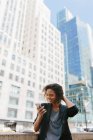 Empresária afro usando telefone inteligente em frente a prédios de escritórios na cidade — Fotografia de Stock