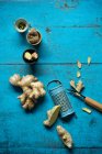 Radice di zenzero, grattugia, tazze piccole e coltello da cucina sdraiato su una superficie di legno blu — Foto stock