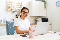 Mulher sorridente sentada à mesa com laptop em casa — Fotografia de Stock