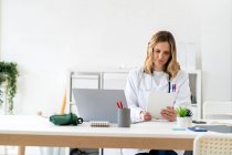 Trabajadora de la salud usando tableta mientras está sentada en el escritorio en la clínica médica - foto de stock