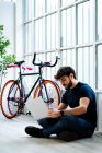 Uomo che utilizza il computer portatile mentre seduto vicino alla finestra in bicicletta a casa — Foto stock