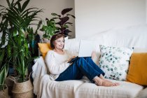 Smiling woman using laptop while sitting on sofa at home — Stock Photo