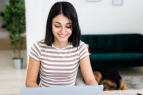 Smiling young woman using laptop while sitting at table in living room — Stock Photo