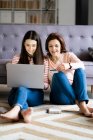 Smiling daughter paying bills online while sitting by mother holding credit card at home — Stock Photo