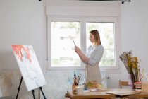 Женщина-художник фотографирует картину через смартфон, стоя в домашней студии — стоковое фото