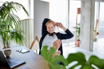 Mujer empresaria sonriente con las manos detrás de la cabeza relajándose en la silla en el escritorio en la oficina en casa - foto de stock