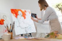 Женщина-художник фотографирует картину в домашней студии — стоковое фото