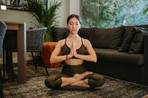 Beautiful woman meditating with clasped hands in living room at home — Stock Photo