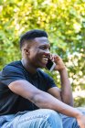 Усміхнений молодий чоловік розмовляє по смартфону, сидячи в парку — стокове фото