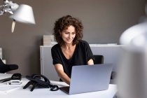Smiling businesswoman working on laptop while sitting at desk in office — Stock Photo