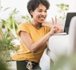 Smiling woman showing peace gesture on video call through digital tablet while sitting at home — Stock Photo