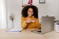 Young woman with credit card using laptop while sitting at home office — Stock Photo