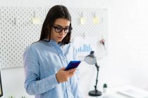 Businesswoman using mobile phone while standing at office — Stock Photo
