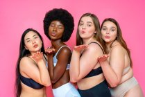 Мультиетнічна група жіночих моделей у білизні, яка випускає поцілунки на рожевому тлі. — стокове фото