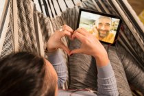 Mature woman showing heart shape sign on video call to man through digital tablet — Stock Photo